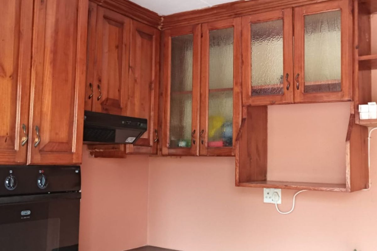 A kitchen area featuring traditional wooden cabinetry, glass-fronted display units, a built-in oven, and an extractor fan, offering a classic aesthetic.