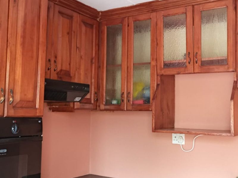 A kitchen area featuring traditional wooden cabinetry, glass-fronted display units, a built-in oven, and an extractor fan, offering a classic aesthetic.