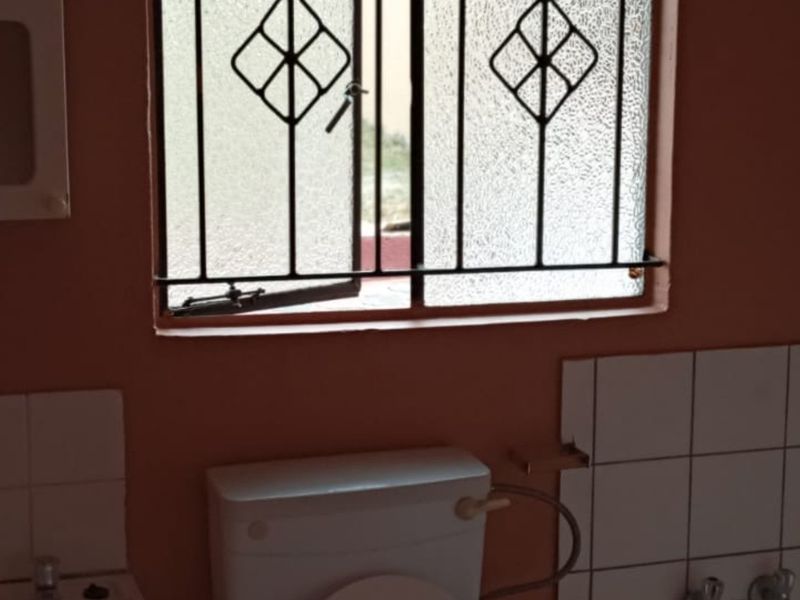 A functional bathroom featuring a toilet, tiled splashback, and a window with security bars, offering a blank canvas for potential modernization.