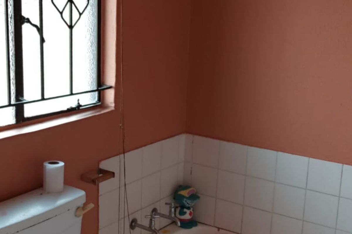 A functional bathroom featuring a bathtub, toilet, and security bars on the window, with dated wall finishes and tiling.