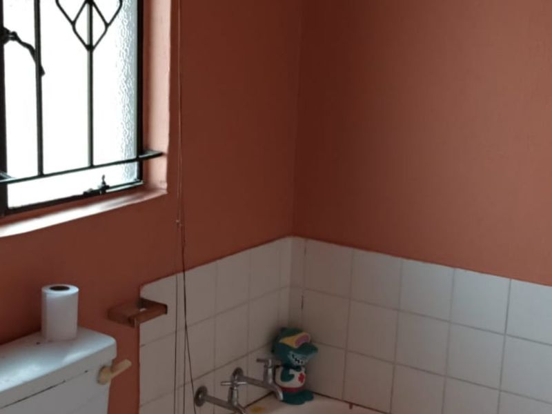 A functional bathroom featuring a bathtub, toilet, and security bars on the window, with dated wall finishes and tiling.