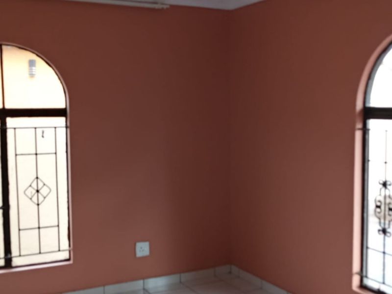 An empty bedroom featuring terracotta-colored walls, tiled flooring, and two arched windows fitted with security bars.