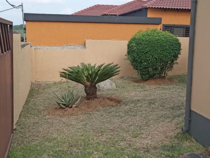 A side garden area featuring a boundary wall, metal gate, and established shrubs, requiring some landscaping maintenance to improve the overall presentation.