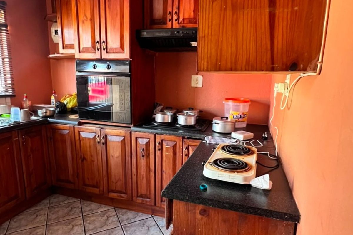 A functional kitchen featuring traditional wooden cabinetry, built-in oven, extractor fan, and granite countertops with tiled flooring.