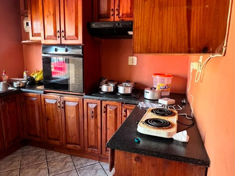A functional kitchen featuring traditional wooden cabinetry, built-in oven, extractor fan, and granite countertops with tiled flooring.