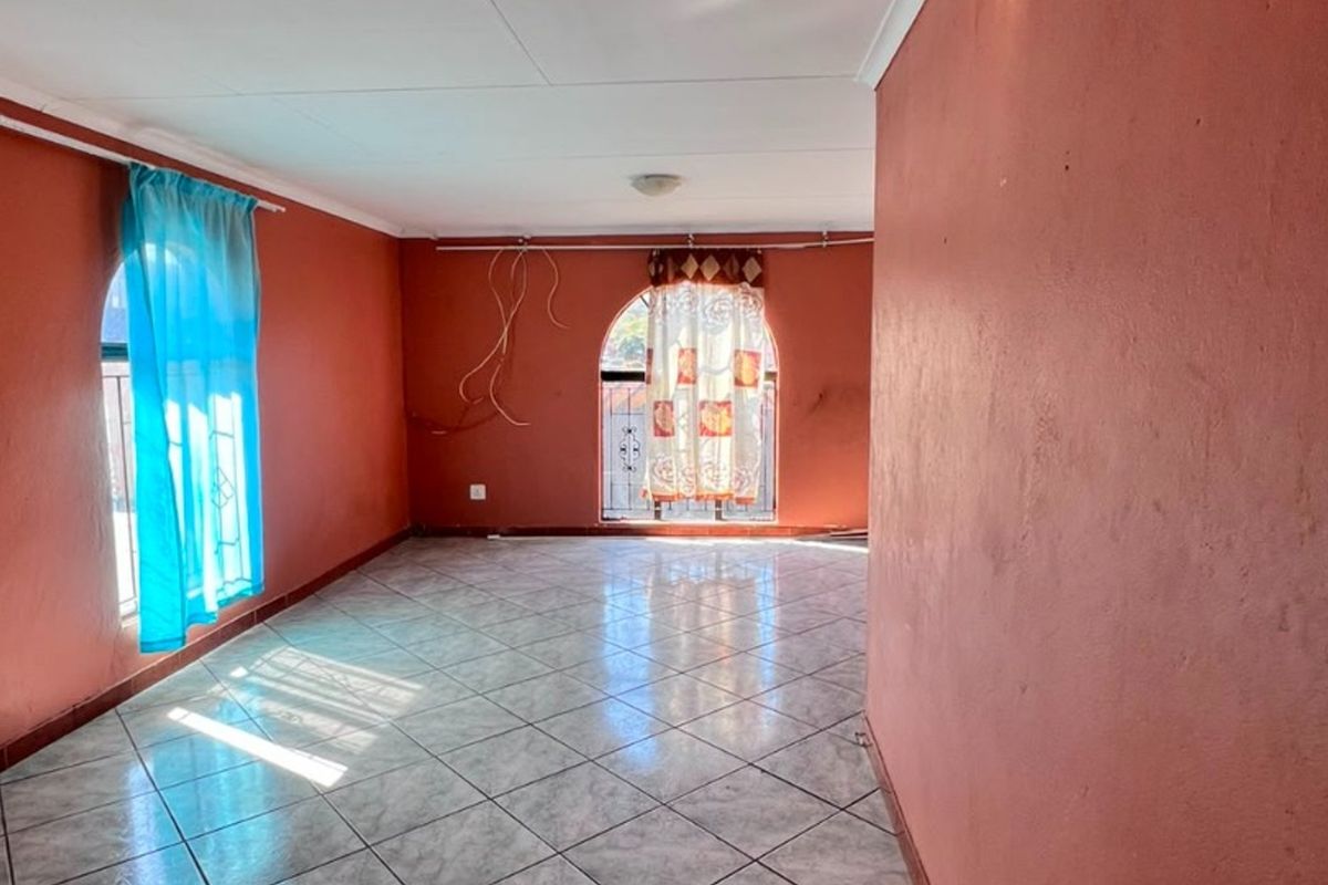 An empty living area featuring tiled flooring and arched windows with security bars, requiring minor cosmetic updates and electrical finishing.