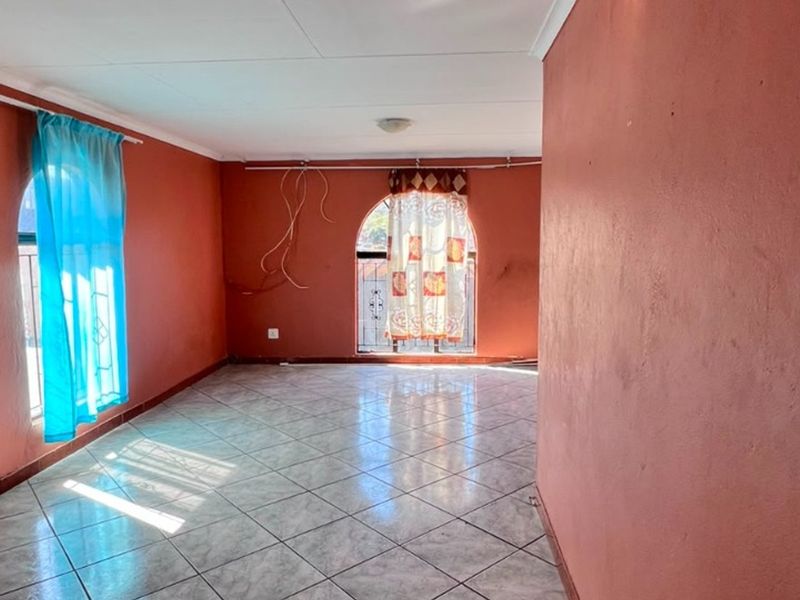 An empty living area featuring tiled flooring and arched windows with security bars, requiring minor cosmetic updates and electrical finishing.