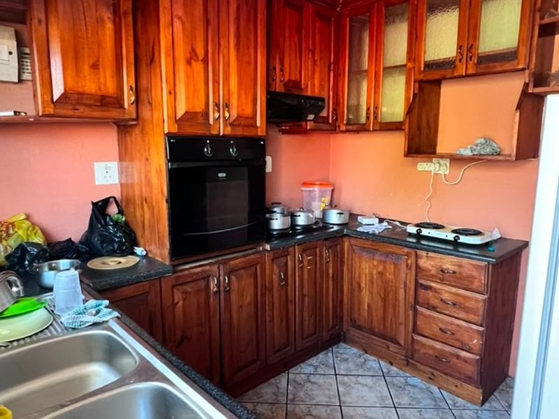 A dated kitchen featuring wooden cabinetry, built-in oven, extractor fan, and double bowl sink with tiled flooring.