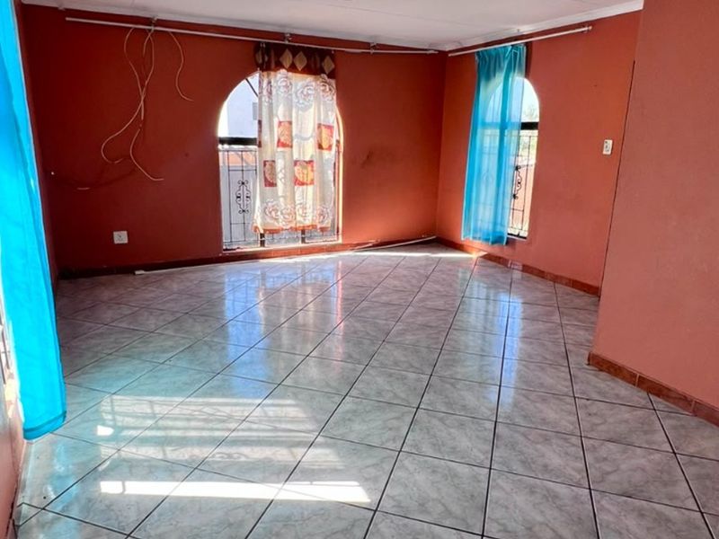 An empty living room featuring tiled flooring and distinctive arched windows with security bars, requiring minor cosmetic updates and electrical finishing.