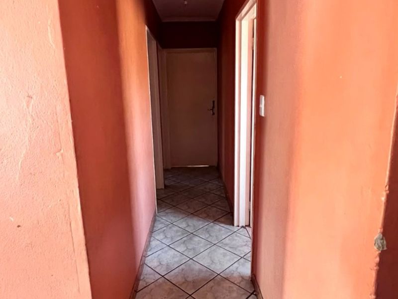A narrow residential hallway featuring tiled flooring and multiple internal doorways, currently vacant and awaiting cosmetic updates.