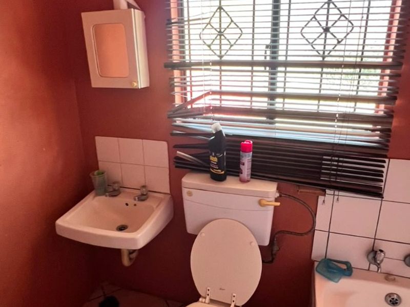 A compact bathroom featuring a wall-mounted basin, toilet, and bathtub with tiled splashbacks and venetian blinds.