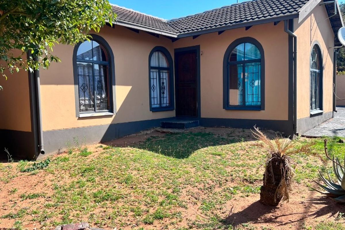 Rear view of the house featuring arched windows with security bars, a tiled roof, and a garden area with exposed soil.