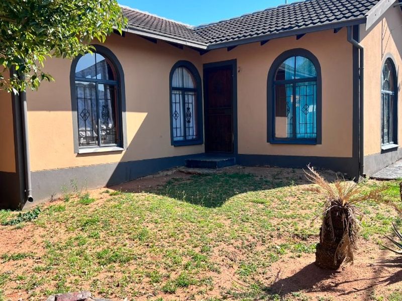 Rear view of the house featuring arched windows with security bars, a tiled roof, and a garden area with exposed soil.