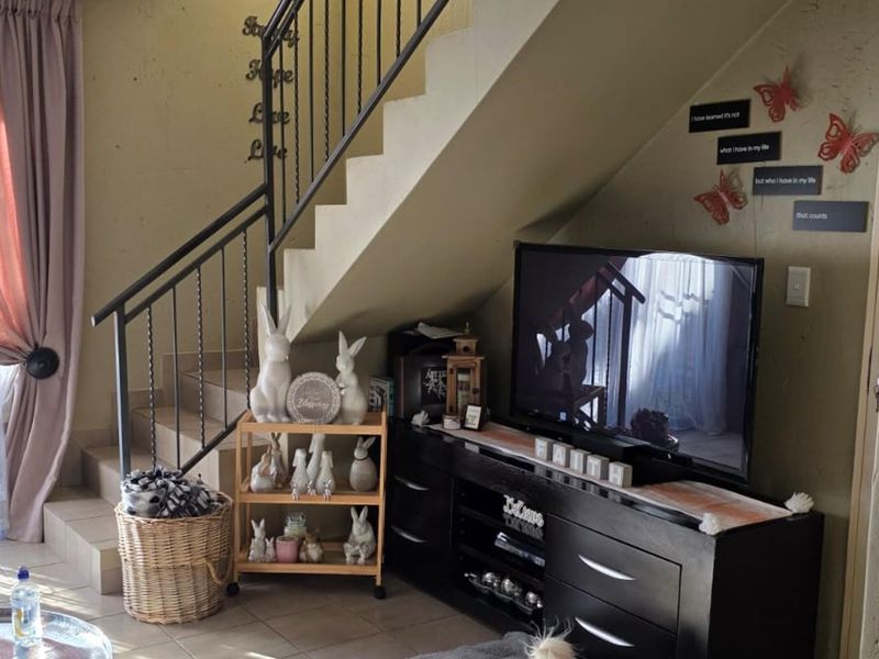 A living room area featuring a staircase with a wrought iron balustrade and tiled flooring, providing a functional space under the stairs.