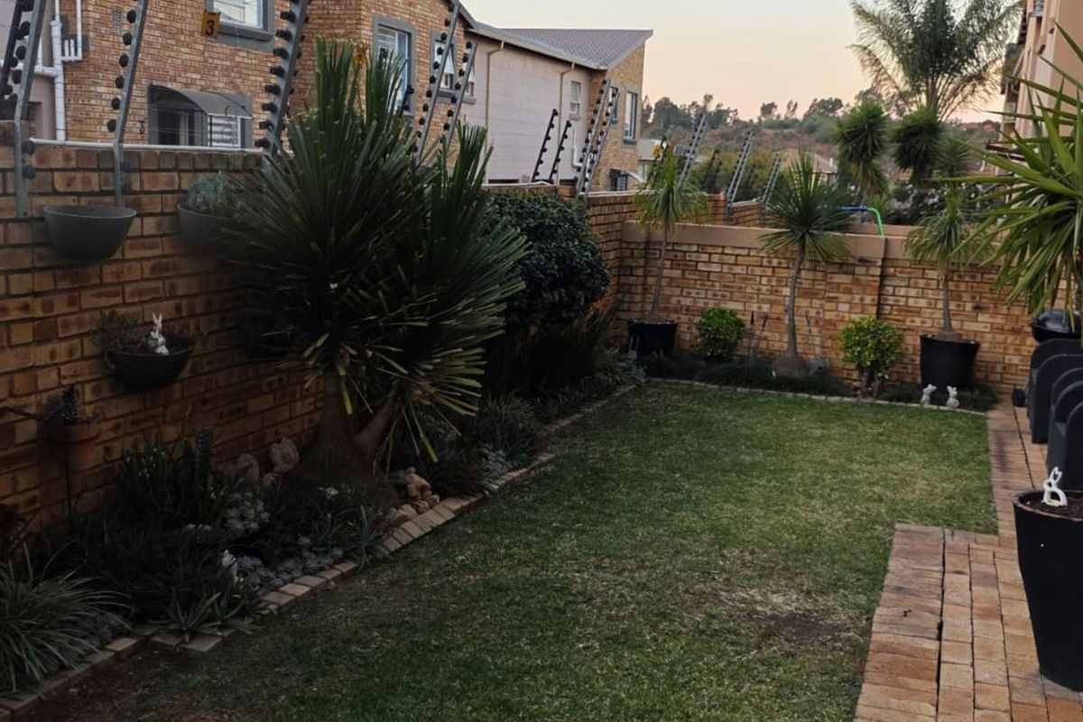 A private rear garden featuring a well-maintained lawn, paved walkway, and secure face brick boundary walls topped with electric fencing.