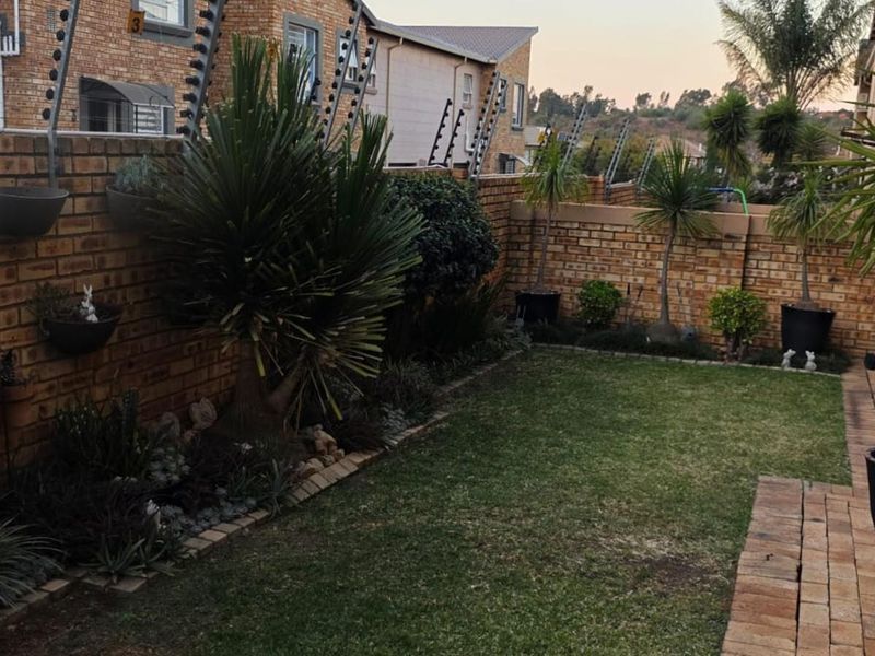 A private rear garden featuring a well-maintained lawn, paved walkway, and secure face brick boundary walls topped with electric fencing.