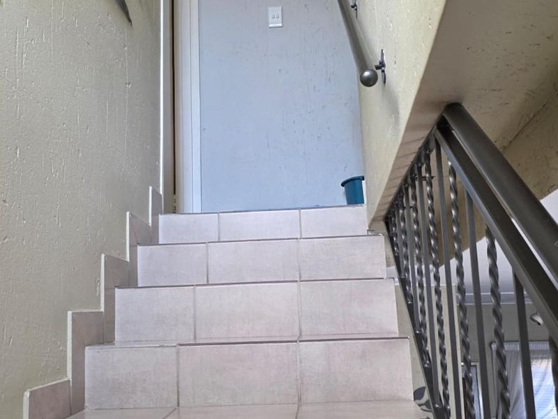 A staircase featuring tiled steps, a metal handrail, and a decorative wrought iron balustrade leading to an upper level.
