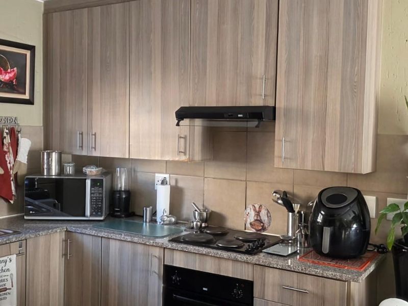 A functional kitchen featuring wood-look laminate cabinetry, granite countertops, a built-in oven, electric hob, and a tiled backsplash.