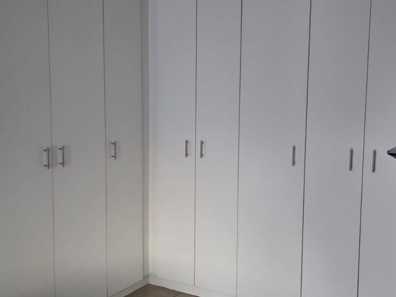 A bedroom featuring extensive white built-in cupboards providing ample storage space.