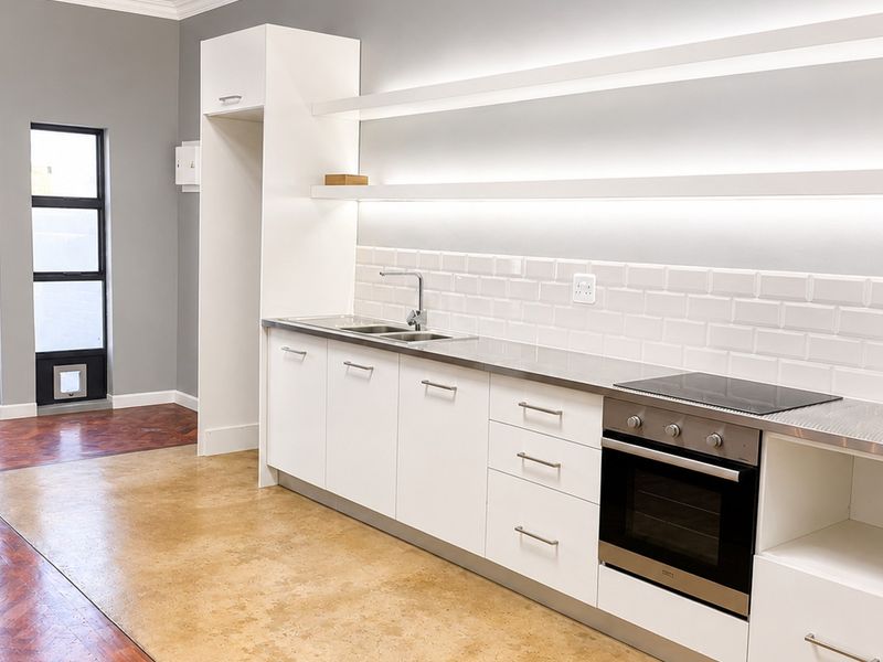Modern kitchen featuring white cabinetry, stainless steel countertops, subway tile backsplash, integrated oven, cooktop, and floating shelves with integrated LED lighting.