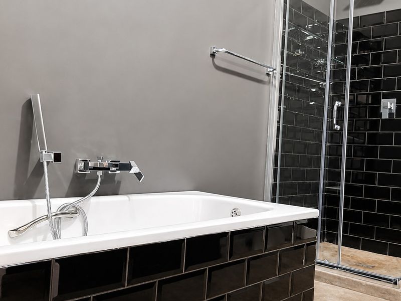 Modern bathroom featuring a built-in bathtub with chrome fixtures and a separate glass-enclosed shower with black subway tile detailing.