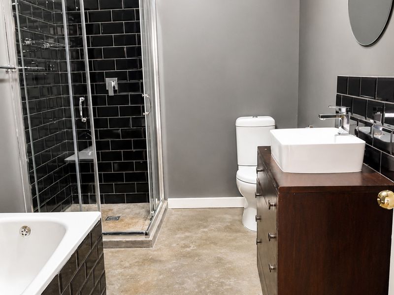 Modern bathroom featuring a glass shower enclosure with black subway tiles, a vessel sink vanity, and a separate bathtub with polished concrete flooring.