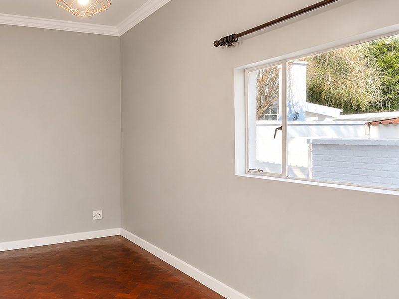 A bright, empty bedroom featuring classic herringbone parquet flooring, crown molding, and a large window overlooking the exterior.