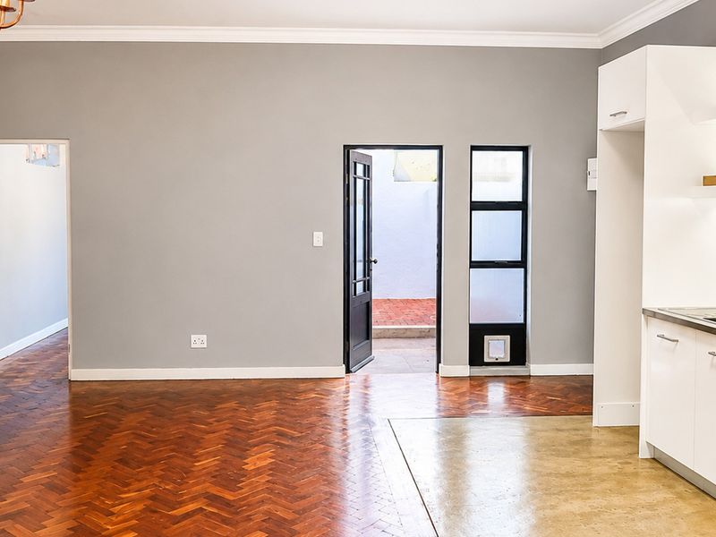 Spacious open-plan living area featuring polished herringbone parquet and concrete flooring, complemented by a modern kitchen with white cabinetry and subway tile backsplash.