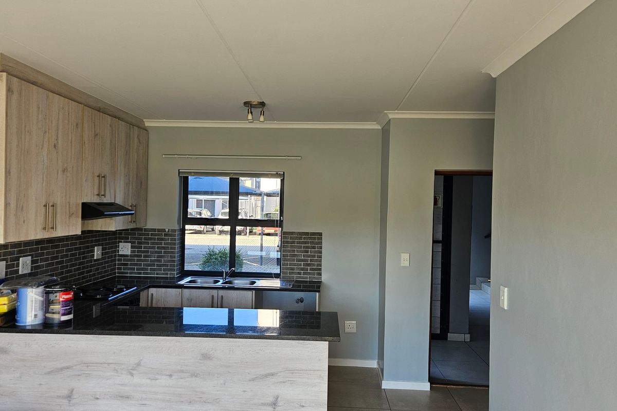 Modern kitchen featuring light wood-finish cabinetry, dark granite countertops, a tiled backsplash, and a functional breakfast bar layout.