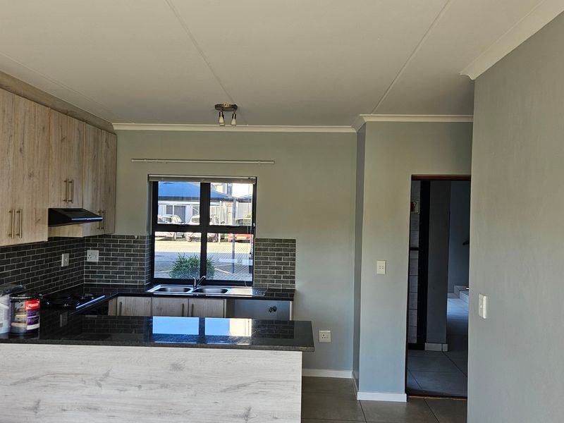 Modern kitchen featuring light wood-finish cabinetry, dark granite countertops, a tiled backsplash, and a functional breakfast bar layout.
