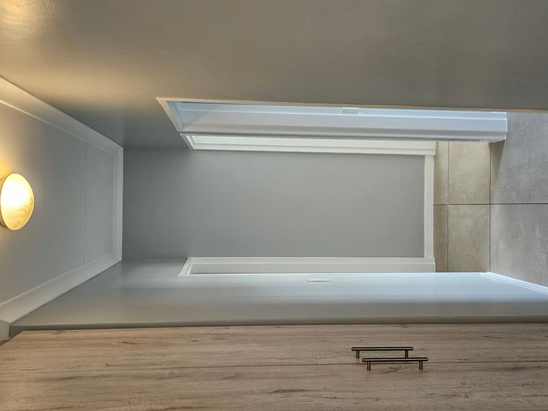 A clean, modern hallway featuring neutral wall tones, built-in cabinetry with contemporary handles, and large format floor tiles.