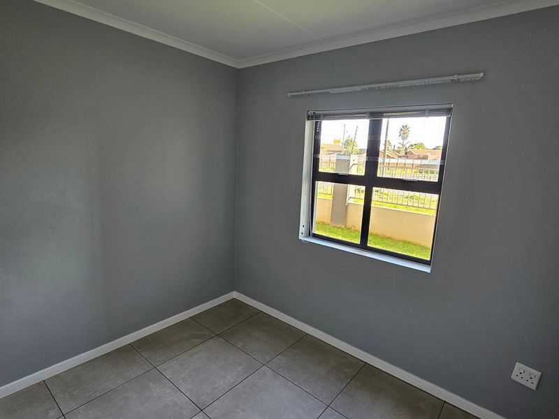 A clean, empty bedroom featuring neutral grey walls, tiled flooring, and an aluminium-framed window with a curtain rail.