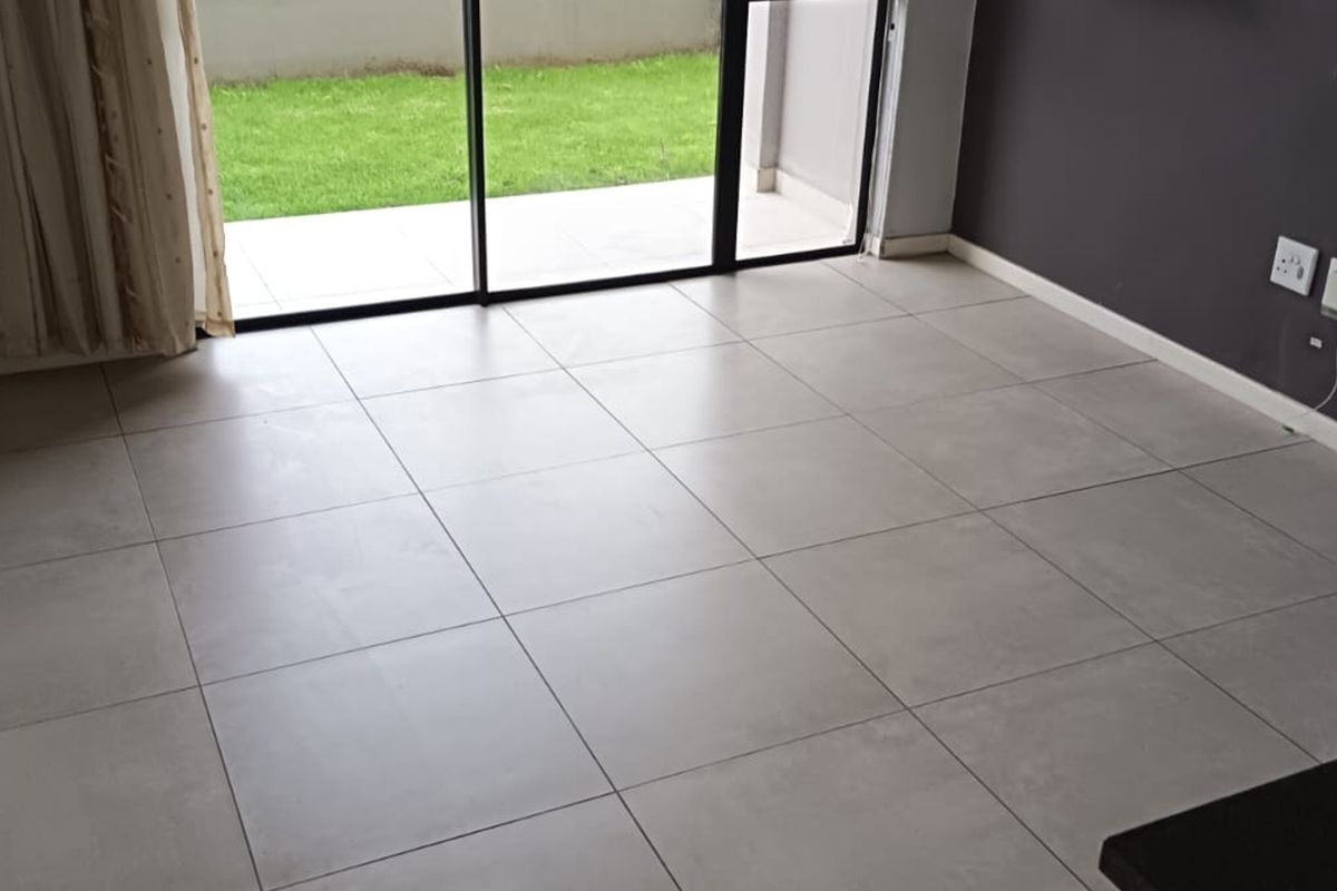 A bright, empty living area featuring large format floor tiles, a dark accent wall, and sliding glass doors leading to an outdoor patio space.