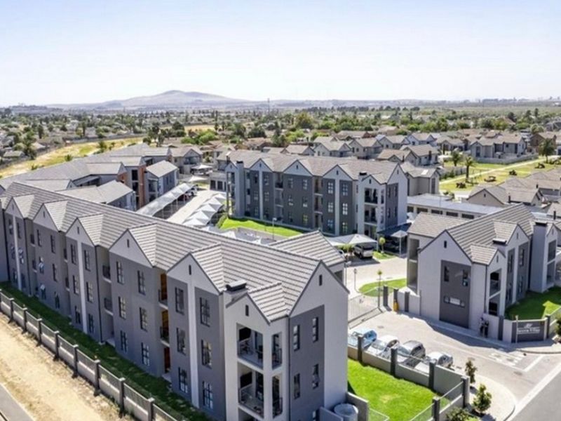 Aerial view of a modern apartment complex featuring multi-story residential buildings, paved parking areas, and landscaped grounds within a secure estate.