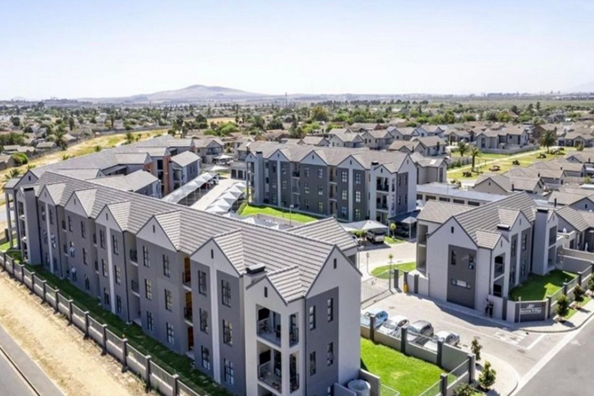 Aerial view of a modern apartment complex featuring multi-story residential buildings, paved parking areas, and landscaped grounds within a secure estate.