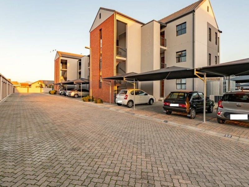 Exterior view of a modern multi-story apartment complex featuring paved parking areas and covered carports.