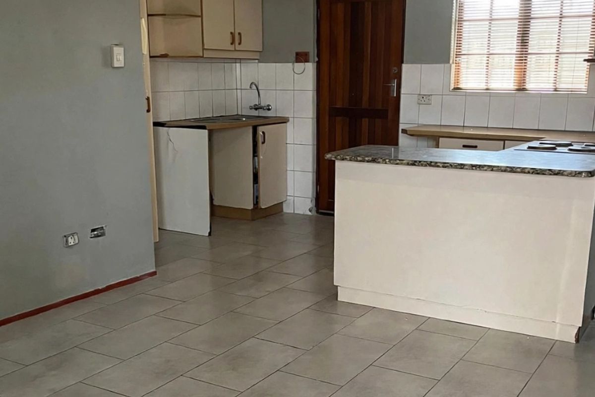 A dated kitchen area featuring built-in cabinetry, a stone countertop, and a hob, currently in need of cosmetic updates and repairs.