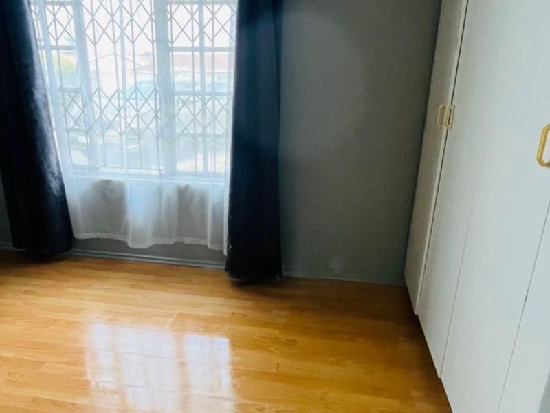 A clean, empty bedroom featuring polished laminate flooring, a built-in wardrobe, and a window fitted with a security gate.