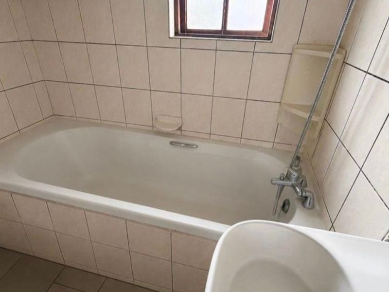 A functional bathroom featuring a standard bathtub with a shower mixer, tiled walls, and tiled flooring, requiring some cosmetic updates.
