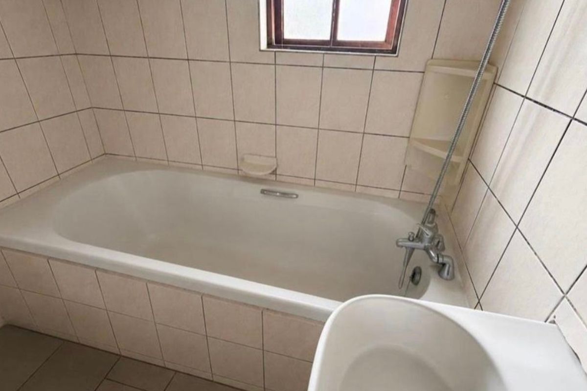 A functional bathroom featuring a standard bathtub with a shower mixer, tiled walls, and tiled flooring, requiring some cosmetic updates.