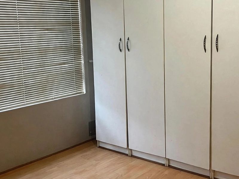 A bedroom featuring built-in cupboards, laminate flooring, and venetian blinds, offering a functional and neutral space ready for personalization.