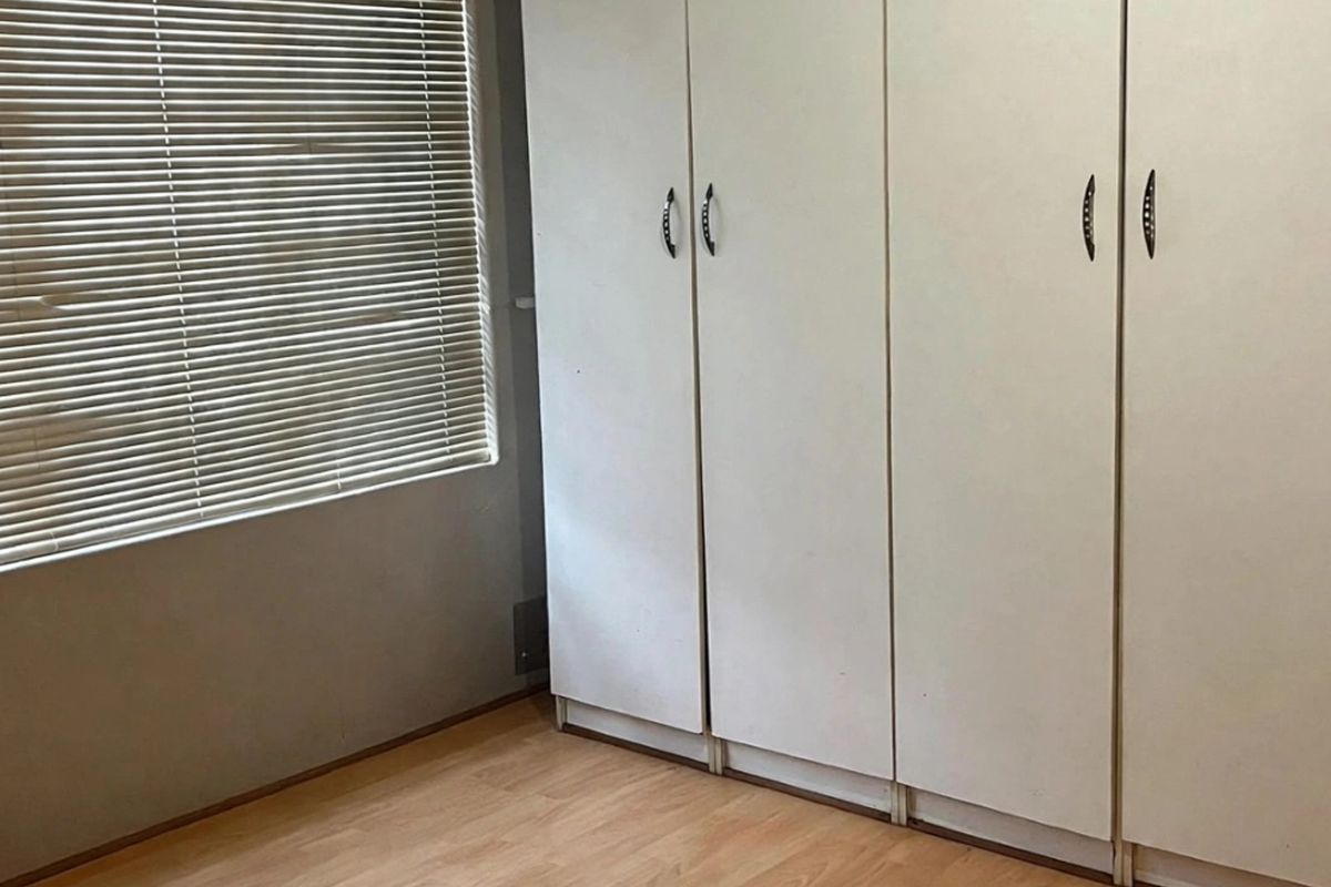 A bedroom featuring built-in cupboards, laminate flooring, and venetian blinds, offering a functional and neutral space ready for personalization.