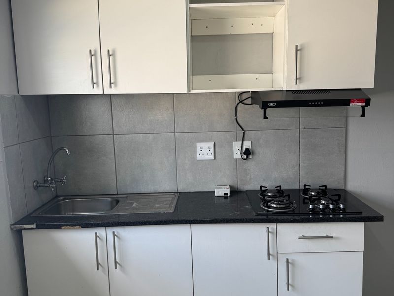 Compact kitchen featuring white cabinetry, a stainless steel sink, gas cooktop, extractor fan, and grey tiled backsplash.