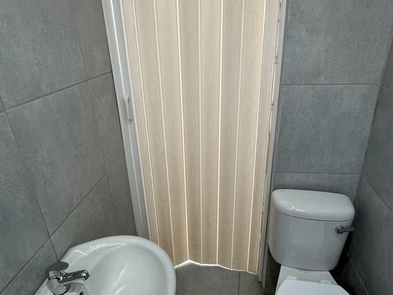 A compact bathroom featuring a pedestal basin, toilet, and neutral grey ceramic tiling throughout.