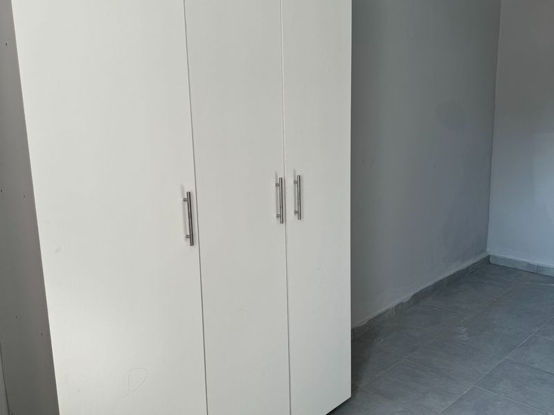 A clean, empty bedroom featuring neutral grey walls, tiled flooring, and a modern white built-in wardrobe with silver handles.