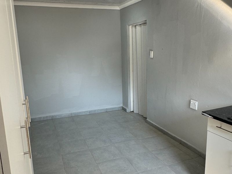 A clean, empty kitchen area featuring grey tiled flooring, recessed lighting, and modern cabinetry with a granite countertop.