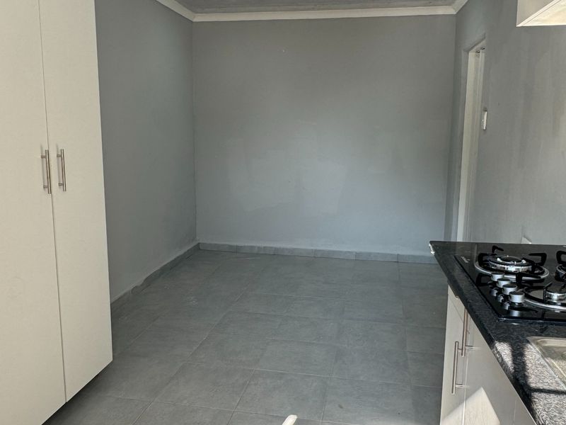 A compact, empty kitchen featuring modern grey floor tiles, built-in white cabinetry, granite countertops, and a fitted gas hob with recessed ceiling lighting.