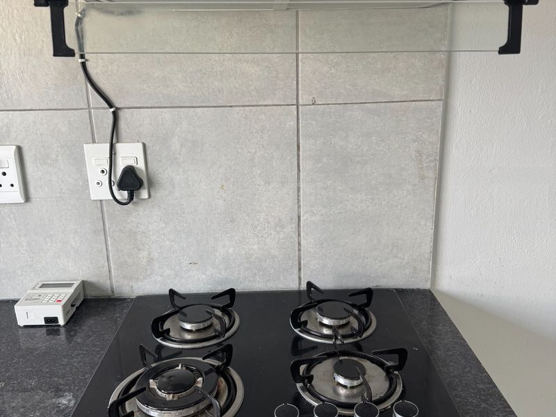 A clean kitchen workspace featuring a modern black gas hob, integrated extractor fan, and durable granite countertops with a neutral tiled splashback.