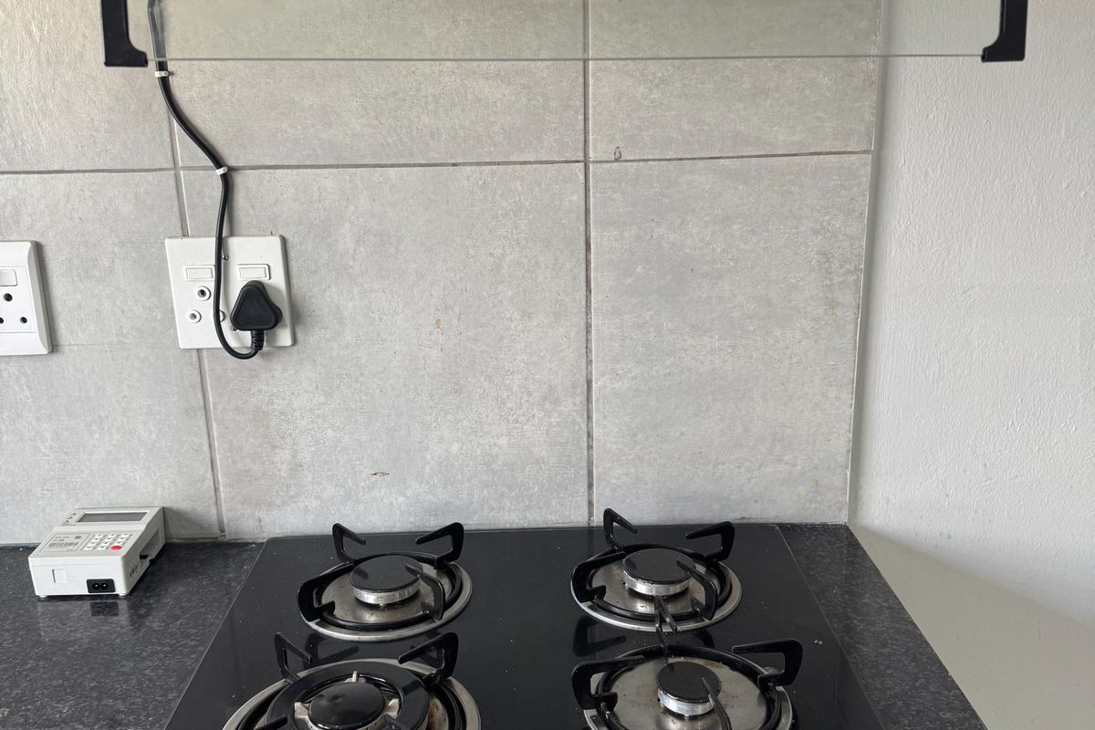 A clean kitchen workspace featuring a modern black gas hob, integrated extractor fan, and durable granite countertops with a neutral tiled splashback.