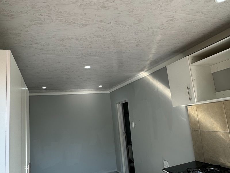 A compact kitchen featuring built-in cabinetry, a gas hob, tiled backsplash, and recessed lighting, currently in an unfinished state.